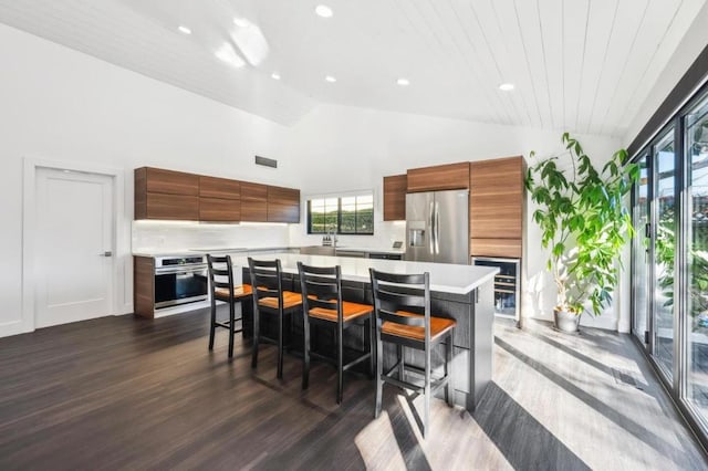 kitchen with dark hardwood / wood-style floors, appliances with stainless steel finishes, a center island, and a kitchen bar