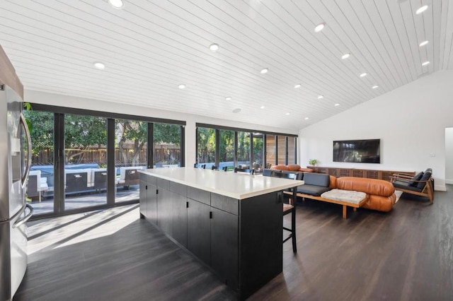 kitchen with dark wood-type flooring, a center island, vaulted ceiling, wooden ceiling, and stainless steel refrigerator