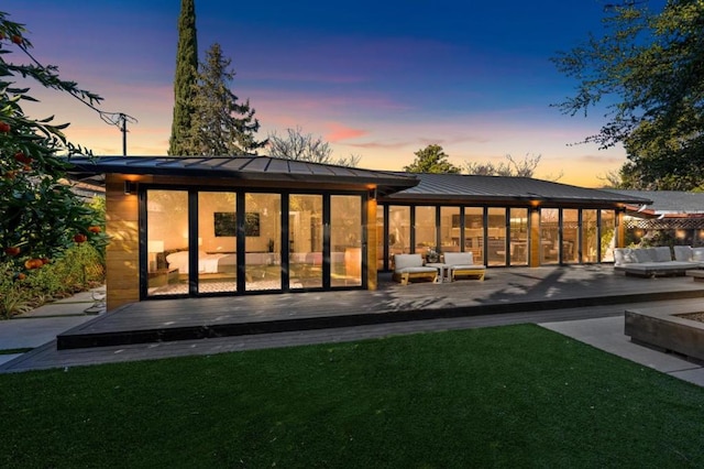 back house at dusk featuring a wooden deck and a lawn