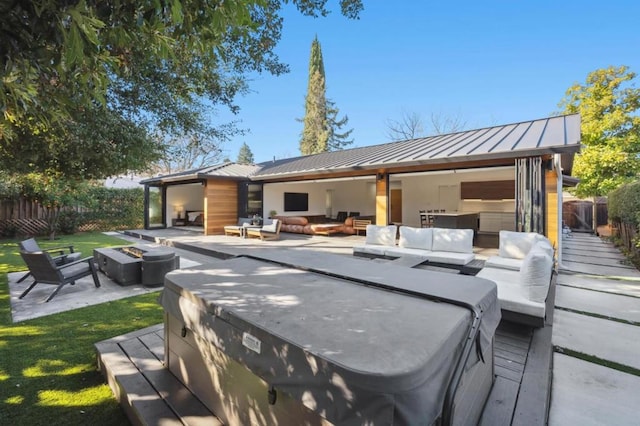 view of patio with a hot tub, a wooden deck, and an outdoor living space with a fire pit