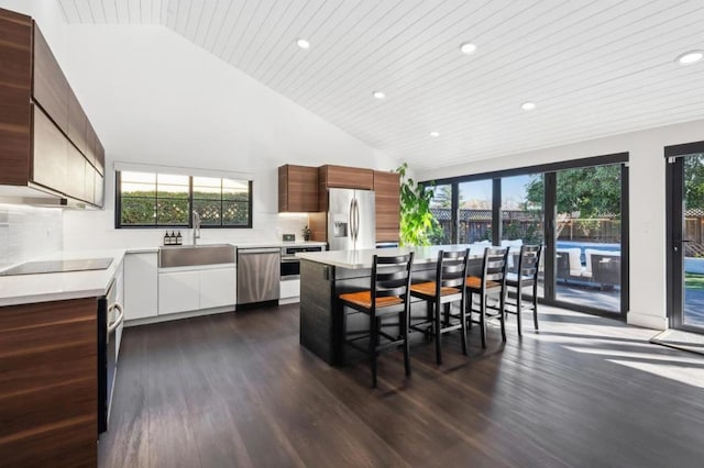 kitchen with sink, dark hardwood / wood-style flooring, a kitchen island, stainless steel appliances, and decorative backsplash