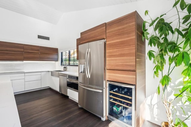 kitchen with high vaulted ceiling, stainless steel appliances, white cabinets, dark hardwood / wood-style flooring, and beverage cooler