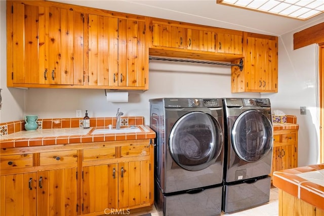 clothes washing area featuring sink, washing machine and dryer, and cabinets