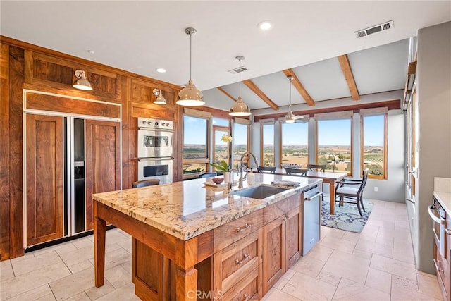 kitchen with sink, light stone counters, an island with sink, pendant lighting, and stainless steel appliances