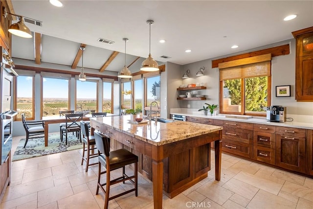 kitchen featuring sink, a kitchen breakfast bar, light stone countertops, a center island with sink, and decorative light fixtures