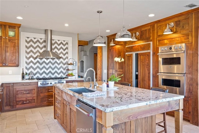 kitchen featuring sink, a kitchen island with sink, light stone counters, stainless steel appliances, and wall chimney exhaust hood