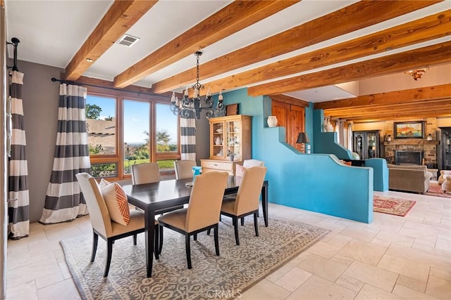 dining area with beam ceiling, a stone fireplace, and a chandelier