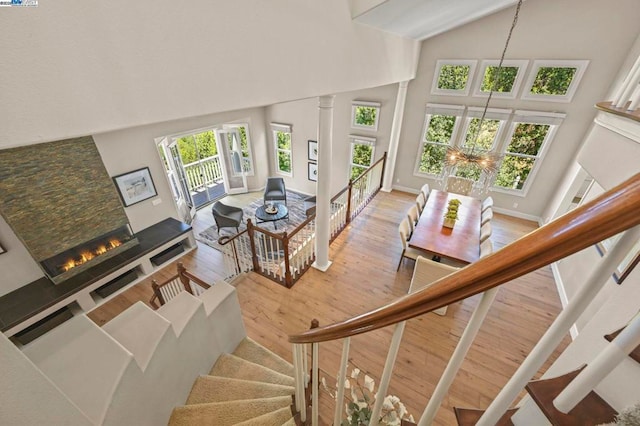 staircase featuring wood-type flooring, a chandelier, high vaulted ceiling, and ornate columns