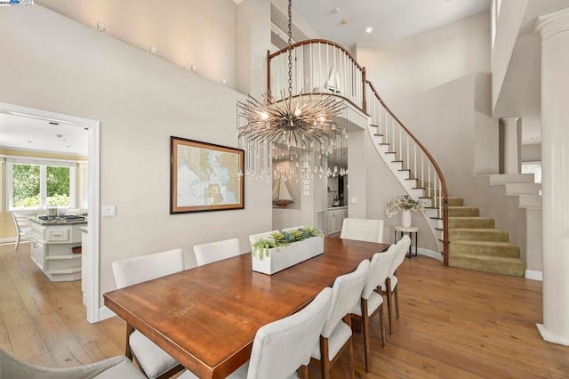 dining space featuring ornate columns, a notable chandelier, a high ceiling, and light wood-type flooring