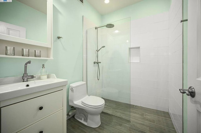 bathroom with hardwood / wood-style flooring, vanity, toilet, and a tile shower