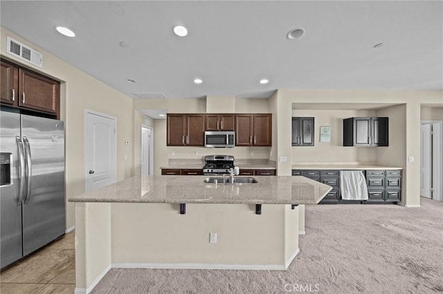 kitchen with a sink, visible vents, a kitchen breakfast bar, appliances with stainless steel finishes, and an island with sink