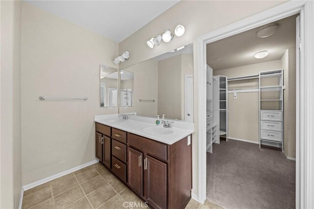 full bathroom featuring double vanity, baseboards, a walk in closet, and a sink