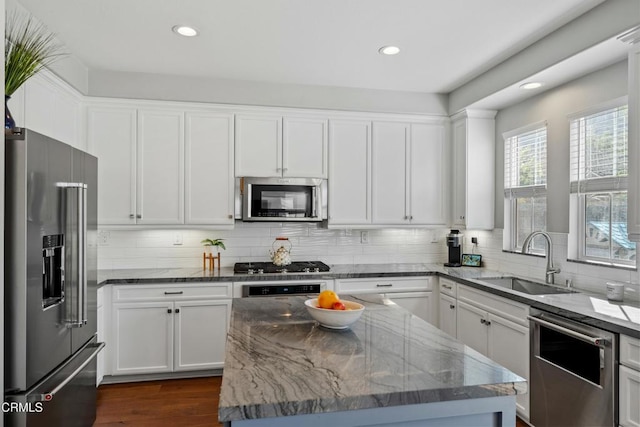 kitchen featuring sink, light stone counters, a center island, stainless steel appliances, and white cabinets