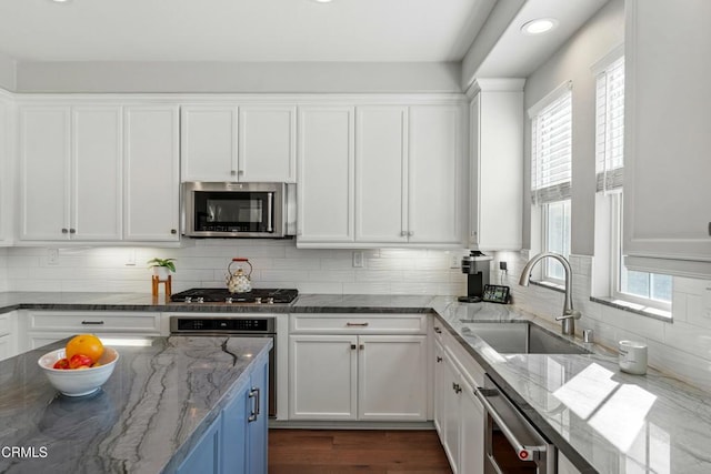 kitchen with sink, white cabinetry, stainless steel appliances, light stone countertops, and decorative backsplash