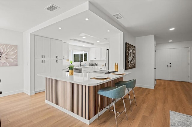 kitchen with a breakfast bar area, white cabinets, black electric cooktop, kitchen peninsula, and light wood-type flooring