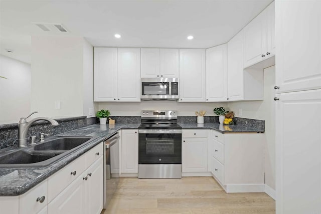 kitchen featuring sink, light wood-type flooring, appliances with stainless steel finishes, dark stone counters, and white cabinets