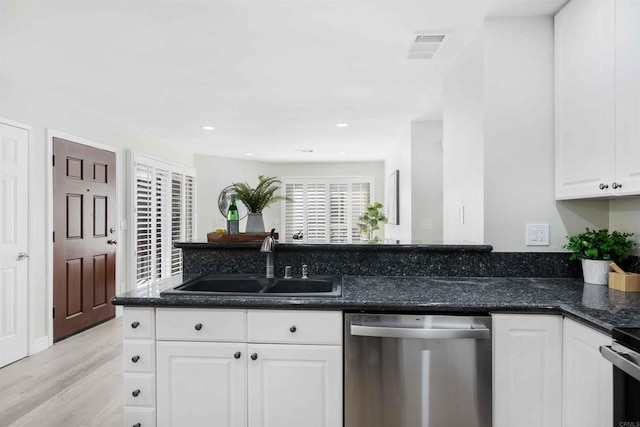 kitchen featuring sink, white cabinetry, dark stone countertops, stainless steel dishwasher, and light hardwood / wood-style floors