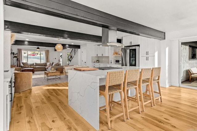 kitchen with a breakfast bar, stainless steel appliances, island range hood, light hardwood / wood-style floors, and white cabinets