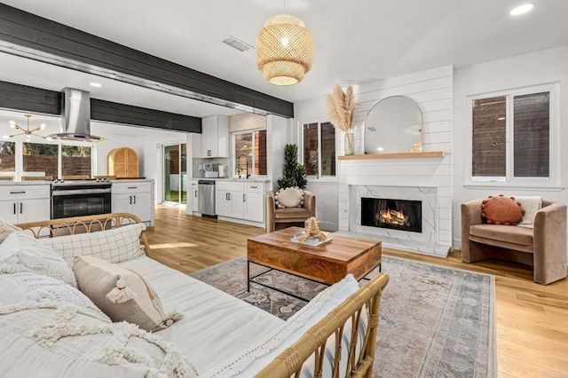 living room with beamed ceiling, sink, a fireplace, and light hardwood / wood-style floors