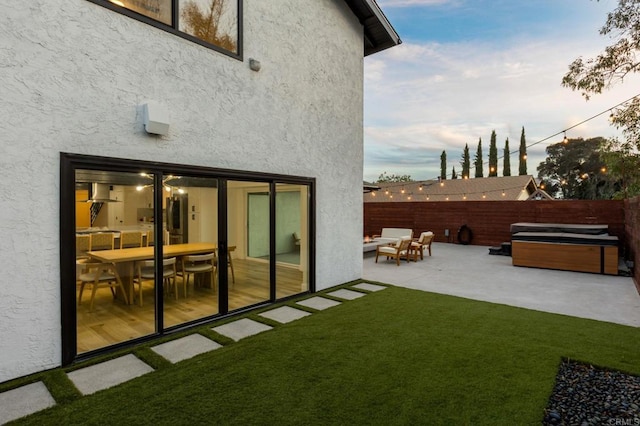 back house at dusk with a yard, a hot tub, and a patio area