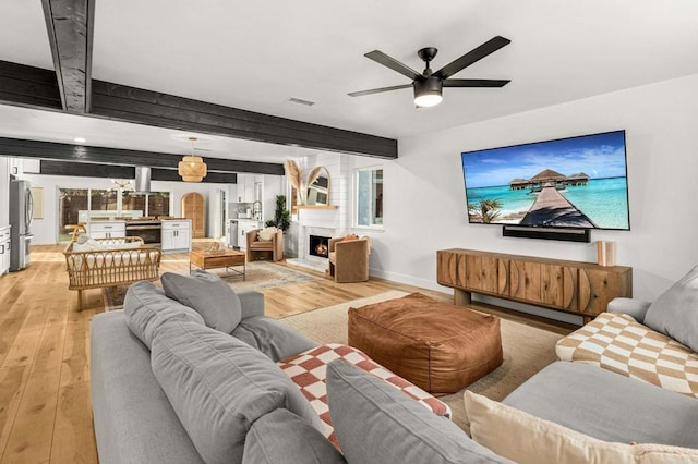 living room featuring beam ceiling, ceiling fan, a large fireplace, and light hardwood / wood-style floors