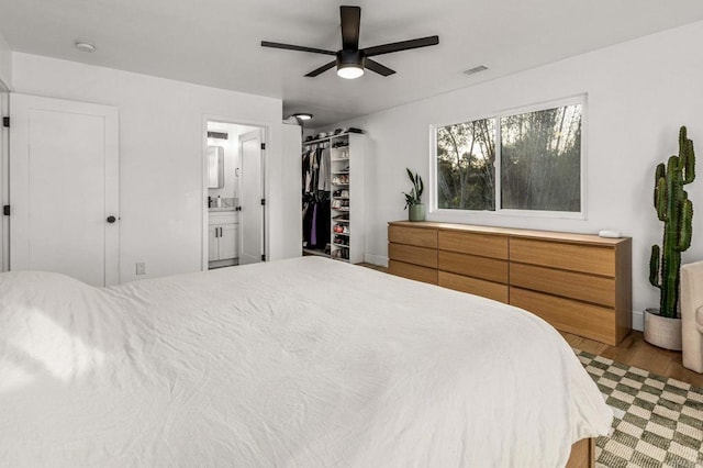 bedroom featuring connected bathroom, light hardwood / wood-style flooring, a spacious closet, ceiling fan, and a closet