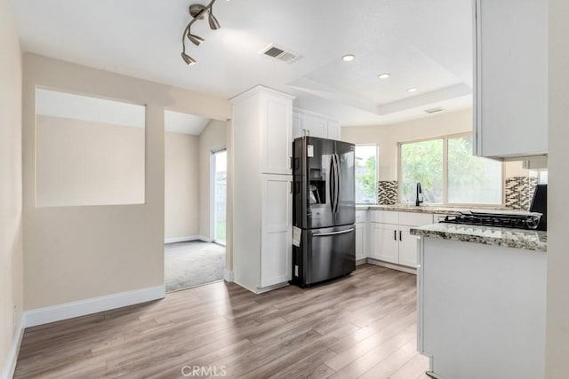 kitchen featuring sink, white cabinetry, stainless steel refrigerator with ice dispenser, tasteful backsplash, and light stone countertops