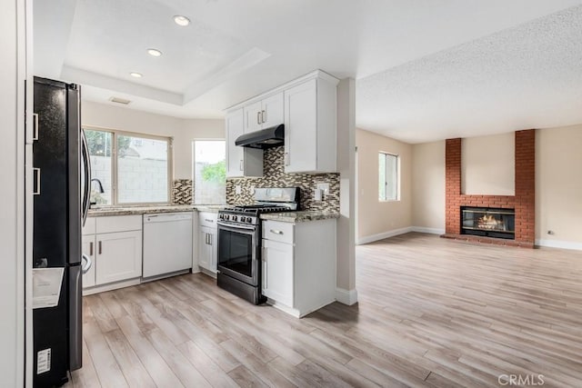 kitchen featuring white cabinetry, stainless steel appliances, a brick fireplace, and backsplash