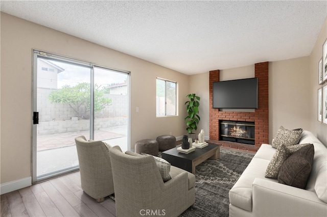 living room with wood-type flooring, a brick fireplace, and a textured ceiling