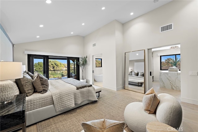 bedroom with high vaulted ceiling, multiple windows, light hardwood / wood-style flooring, and ensuite bath