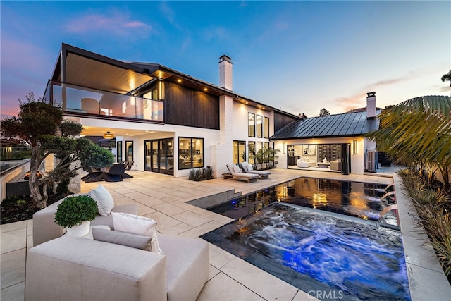 back house at dusk featuring an outdoor hangout area, a balcony, and a patio area