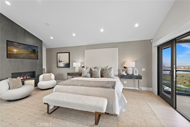 bedroom featuring access to outside, vaulted ceiling, a water view, and a fireplace