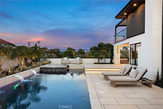 pool at dusk with pool water feature and a patio area