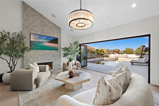 living room featuring high vaulted ceiling, a premium fireplace, a chandelier, and light hardwood / wood-style floors