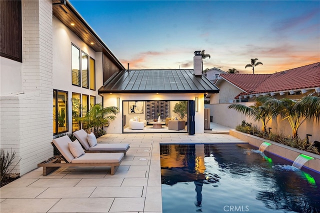 back house at dusk with pool water feature, outdoor lounge area, and a patio area