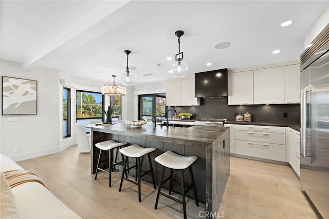 kitchen featuring sink, a kitchen island with sink, white cabinets, and pendant lighting