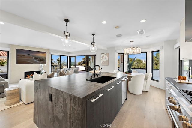 kitchen featuring appliances with stainless steel finishes, pendant lighting, dark brown cabinetry, and a kitchen island with sink