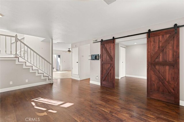 unfurnished living room with dark hardwood / wood-style floors, ceiling fan, and a barn door