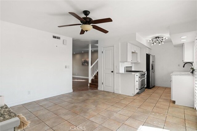 kitchen with sink, appliances with stainless steel finishes, white cabinets, light tile patterned flooring, and ceiling fan with notable chandelier