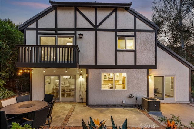 back house at dusk featuring a patio, a balcony, and central AC