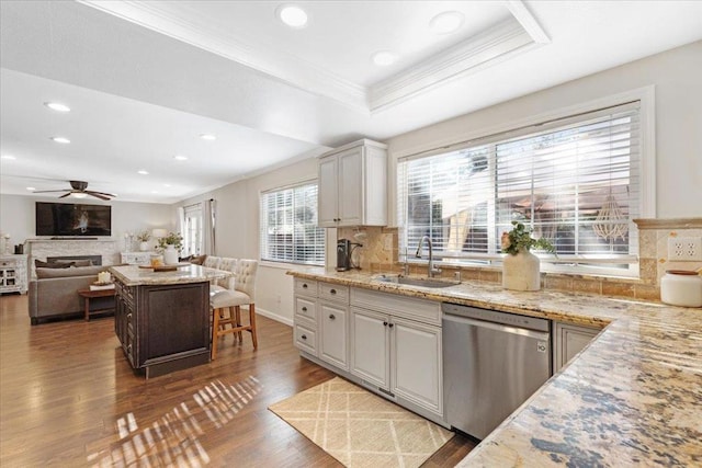 kitchen featuring light stone counters, stainless steel dishwasher, a raised ceiling, and sink