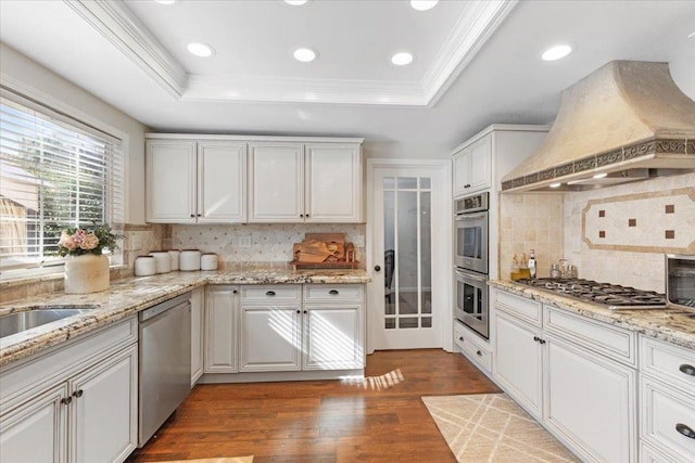 kitchen with custom exhaust hood, white cabinetry, stainless steel appliances, and a tray ceiling