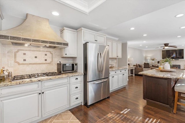 kitchen with custom exhaust hood, appliances with stainless steel finishes, a breakfast bar area, and white cabinets