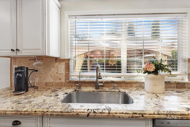 kitchen with tasteful backsplash, dishwasher, sink, white cabinets, and light stone countertops