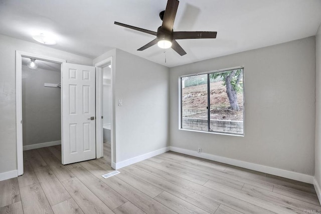 unfurnished bedroom featuring ceiling fan, a walk in closet, a closet, and light hardwood / wood-style flooring