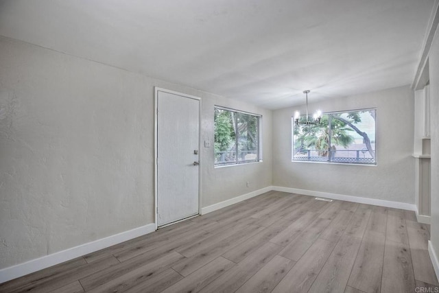 unfurnished room featuring an inviting chandelier, a healthy amount of sunlight, and light hardwood / wood-style floors