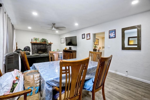 dining room with wood-type flooring, a stone fireplace, and ceiling fan