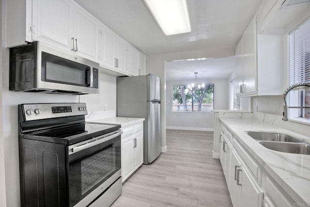 kitchen with sink, appliances with stainless steel finishes, white cabinetry, light stone counters, and light wood-type flooring