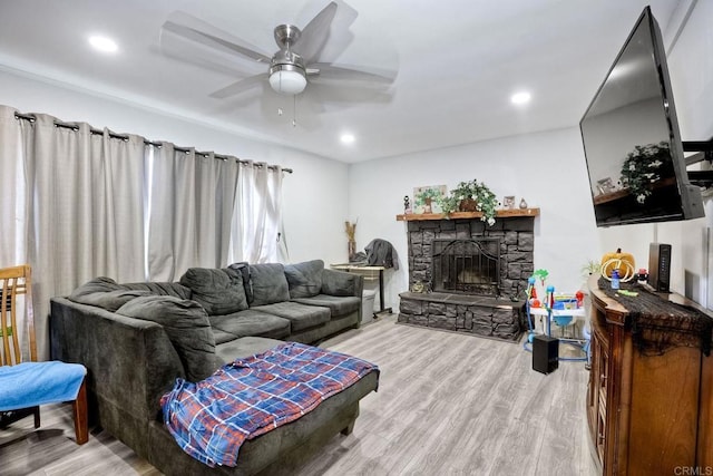 living room featuring ceiling fan, a stone fireplace, and light hardwood / wood-style floors