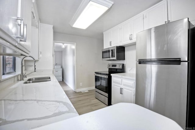 kitchen featuring washer / dryer, sink, white cabinetry, stainless steel appliances, and light stone countertops